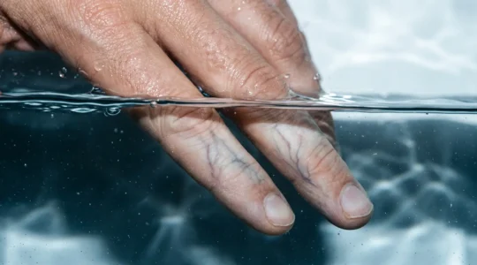 Gros plan macro sur une main humaine dans l'eau froide avec effet de vasoconstriction visible sous la peau